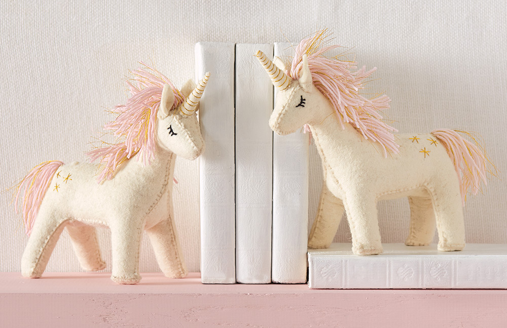 Handmade boiled-wool unicorn bookends with yarn and lurex mane stand with weighted bases to creatively accent a dresser or floating shelf.