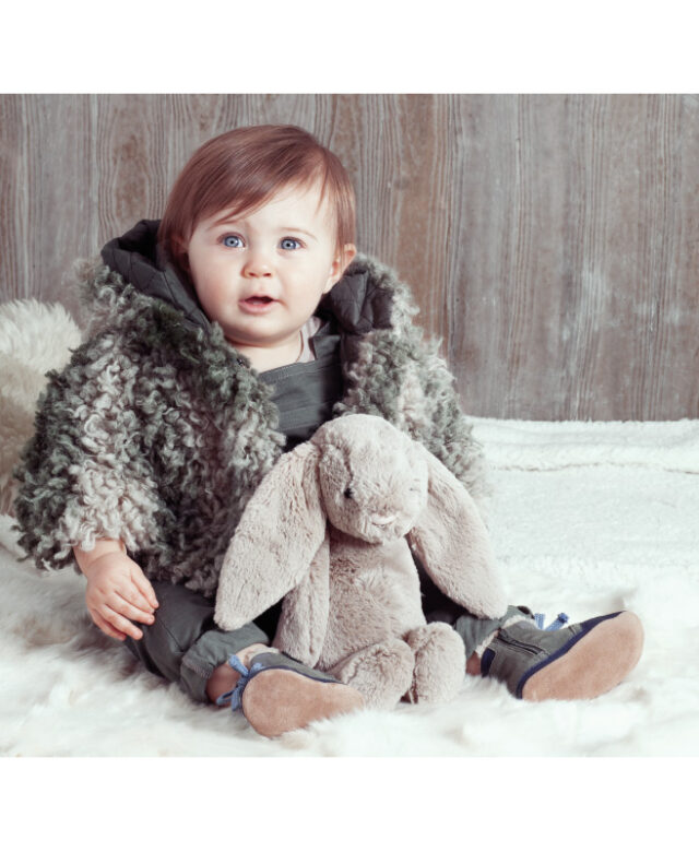 Ava wears Tia Cibani Kids 
shaggy hooded jacket, Robeez crib shoes and Saint Haven one-piece worn underneath Paper Wings overalls.
