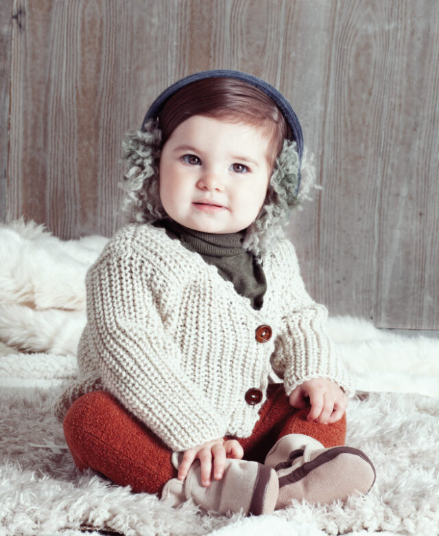 Ava wears Tia Cibani Kids green turtleneck and 
shaggy earmuffs, Oeuf cardigan, leggings by Oh Baby and Robeez booties.
