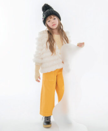 Layla wears Widgeon faux fur fringe jacket, striped shirt and yellow jeans by Molo, Young Soles black shearling lined boots and 
hat by Lola + the Boys.