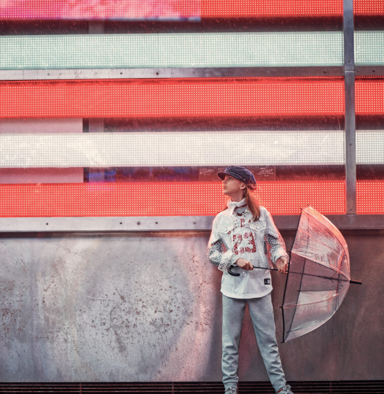 Carly wears Little Lids hat, 
vintage scarf, Nununu long-sleeve shirt, Jordan jersey, Tractr transparent jacket, Tommy Hilfiger pants and stylist’s own umbrella.