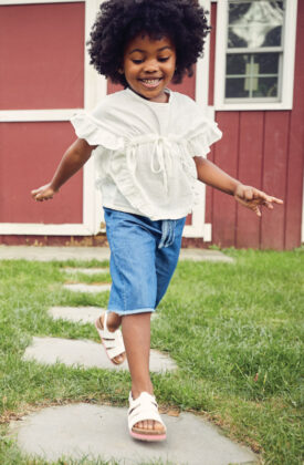 Harper wears Beet World top, cut-off jean shorts by Yellow Sub and Bearpaw white sandals.
