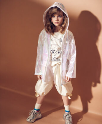 Izzy wears iridescent jacket by American Jewel, graphic tee by Anchors-n-Asteroids, pants by Tia Ciabani, Fun Socks socks and Steve Madden sneakers.