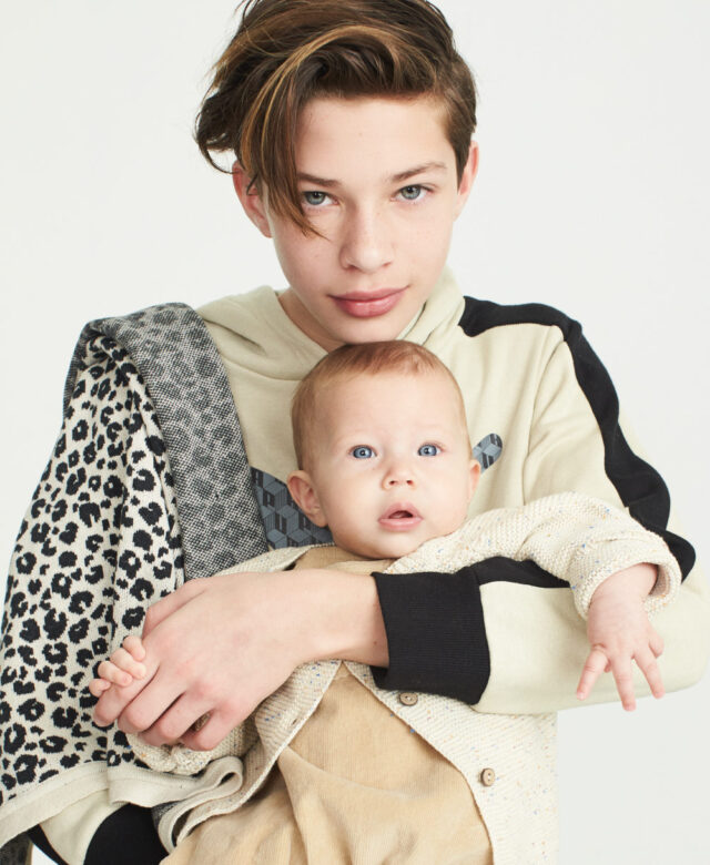 Indy wears Puma wears sweatshirt with Elegant Baby blanket over shoulder; Boheme wears Greige overalls and Huxbaby cardigan.